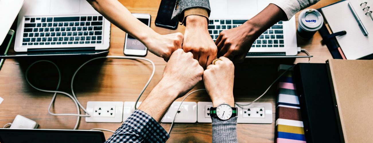 A photo of five hands together over an office table.