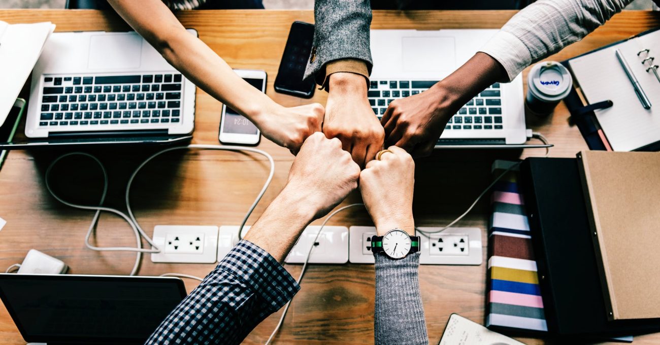 A photo of five hands together over an office table.
